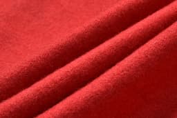 A close-up of red fabric with a soft, textured appearance, featuring folded layers.