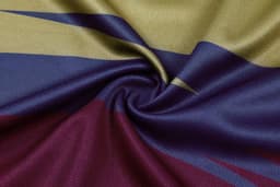 A close-up of micro mesh fabric featuring shades of gold, blue, burgundy, and dark purple, designed with swirling patterns.
