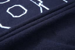 A close-up of a navy collegiate jacket fabric featuring textured lettering and stitched details.