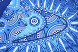 A patterned blue fabric featuring intricate designs and shapes, likely from the Aboriginal Cotton Tee shirt.
