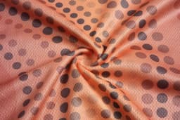 An orange fabric featuring a swirl pattern of black polka dots, showcasing a smooth texture.