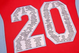 A red hoodie featuring blue accents and large embroidered numbers, with a list of names in the centre.