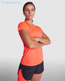 An orange women's T-shirt with a fitted design, paired with black athletic shorts. The model stands confidently.