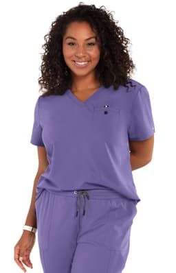 A woman wearing a purple medical scrub top with a pocket and a logo, smiling against a white background.