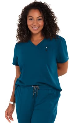 A teal women's top with a V-neck, short sleeves, and a pocket, worn with matching pants. The model has curly hair.