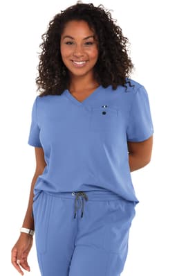 A woman wearing a short-sleeved, blue top with a pocket, part of a scrub set, smiling at the camera.