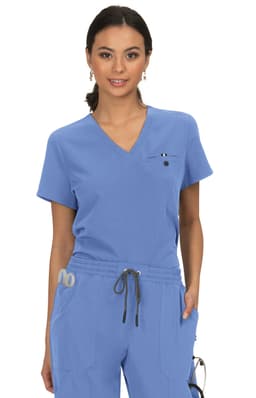 A woman wearing a light blue scrubs top with a v-neck and a small logo on the chest.