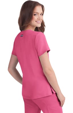 A woman in a pink top stands, smiling over her shoulder. The top has short sleeves and a logo on the back.
