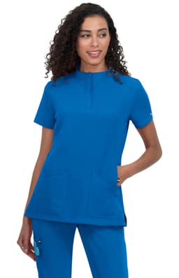 A medical scrub top in bright blue, featuring a neckline zip and two front pockets, worn by a model with curly hair.