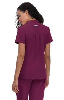 A woman wearing a maroon medical scrub top with short sleeves and a back pleat. The top features a small logo.