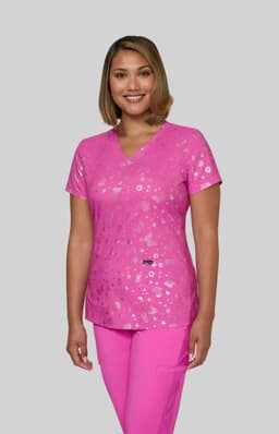 A pink scrub top featuring a floral print, worn by a model. The top has a V-neck and a logo on it.