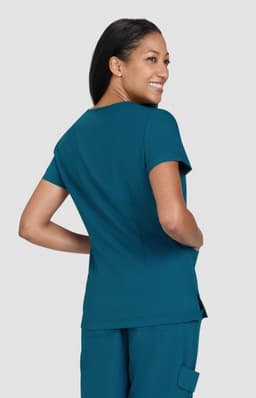A woman is wearing a teal top, looking back with a smile, featuring a fitted design and short sleeves.