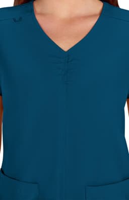 A teal medical scrub top featuring a V-neck design and gathered detailing at the front. It has pockets and a logo.
