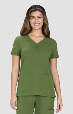 A green scrubs top featuring a V-neck, short sleeves, and two front pockets. The model is smiling.