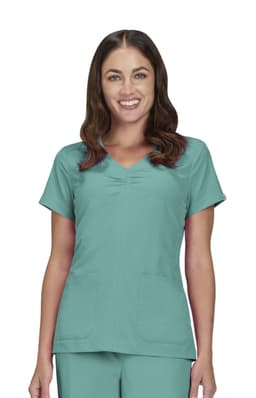 A scrub top in teal featuring short sleeves and two front pockets. The model smiles while wearing the top.