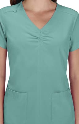 A scrub top in a teal colour with a V-neck and short sleeves, featuring two front pockets and a logo.