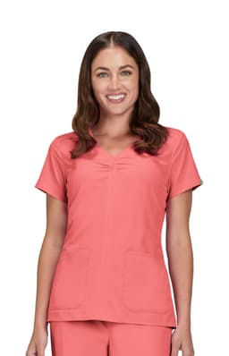A woman wearing a coral scrub top with a scoop neckline and two front pockets.
