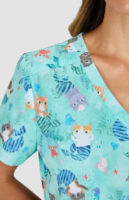 A short-sleeved top in a light teal with a playful animal print featuring cats and marine motifs. It has a branding logo.