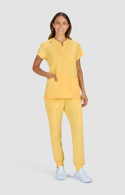 A model in a bright yellow top and matching pants, featuring pockets and a logo. The outfit is paired with white shoes.