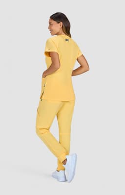 A model wearing a yellow top and matching pants, with white shoes, facing away from the camera.