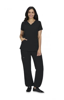 A woman wearing a black scrub top and black pants, standing with one hand in her pocket. The outfit includes a logo.
