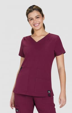 A maroon Sari Top featuring a V-neck and two front pockets, worn by a smiling model. The top has a brand logo.