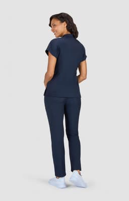 A woman stands wearing a navy blue polo top and matching trousers, with white shoes, facing away from the camera.