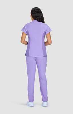 A woman wearing a lilac-coloured scrub set with a short-sleeve top and matching pants, viewed from the back.