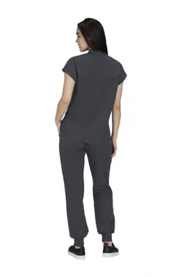 A woman in a grey top and matching grey pants, viewed from the back, wearing casual shoes. A logo is visible.