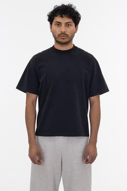 A black short sleeve garment dye t-shirt worn by a person, paired with light grey pants, featuring a logo.