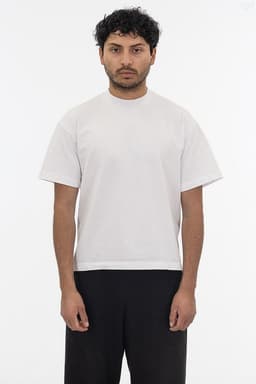 A short sleeve garment dye t-shirt in a light colour, featuring a logo, worn by a model standing against a plain background.