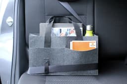 A grey organiser bag with handles, featuring pockets for documents and a drink bottle, sits on a vehicle seat.