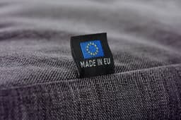 A close-up of a grey fabric showing a label with a flag and the text "MADE IN EU".