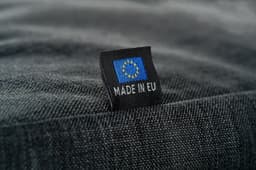 A close-up of a textured black fabric bag showcasing a small tag with a logo and "MADE IN EU".