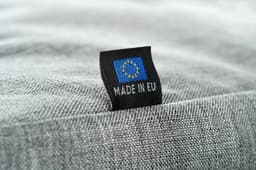 A grey fabric featuring a tag with a logo and the text "Made in EU."