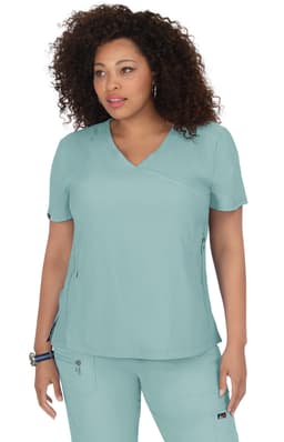 A woman models a teal scrub top, featuring a V-neck and short sleeves, with a logo on one side.
