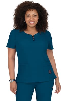 A woman wearing a teal medical scrub top with a round neckline and two front pockets. The top features a logo.