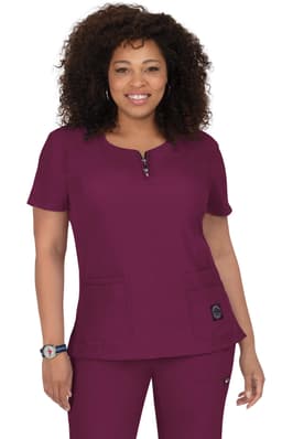 A woman wearing a short-sleeved scrub top in deep burgundy with a round neckline and pockets. The top has a logo.