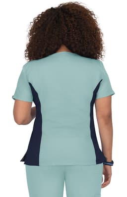 A back view of a turquoise scrub top featuring navy side panels and short sleeves. The garment has a branding logo.