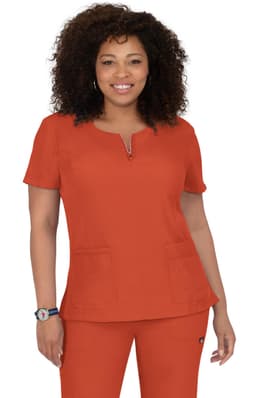 A woman in a bright orange scrubs top with short sleeves, featuring a zipper and two front pockets, stands smiling.