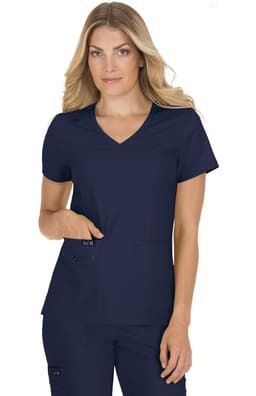 A woman wearing a navy blue medical scrub top with a V-neck and two front pockets. The top has a branding logo.
