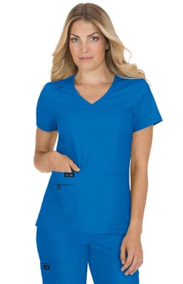 A woman models a blue scrubs top with a V-neck design and pockets, featuring a branding logo.