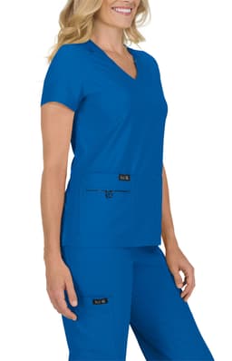 A woman wearing a blue scrub top with a v-neckline, paired with matching blue scrub pants. The outfit features pockets.