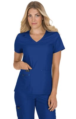 A woman models a blue medical scrub top with a v-neck and pockets, featuring a logo on the sleeve.