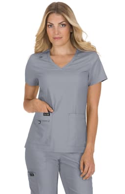 A woman in a grey scrubs top with pockets, posing with hand in pocket. The top has a logo on it.