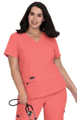 A model wearing a coral scrub top with a V-neck and two front pockets, holding a stethoscope.