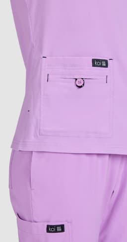 A lilac top featuring a front pocket with a button, alongside matching lilac pants, both with a brand logo.