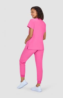 A model wearing a bright pink two-piece outfit, consisting of a top and fitted pants, paired with white footwear.