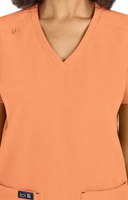 A scrub top in a soft orange colour with a V-neck design and a logo at the bottom.