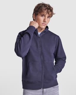 A navy hooded sweatshirt featuring a zip closure and front pockets, modeled by a young man. It has a logo on it.